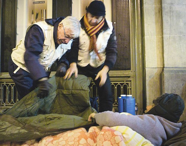 Szociális munkások segítenek egy hajléktalannak Párizsban