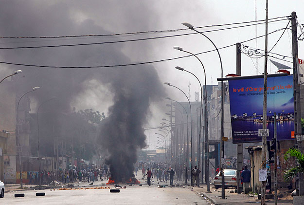 People walk near smoke rising from burning tyres at a street in Abidjan December 16, 2010. Heavy weapons were fired near the Abidjan base of the internationally-endorsed winner of a disputed presidential poll on Thursday before a planned march by his