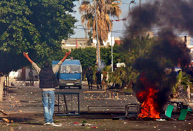 A felgyújtott barikád mellől kiabál a rendőröknek egy tüntető a Tunézia középső részén fekvő Regueb városában. A maghrebi zavargásokat többen a 2011-re jósolt éhséglázadások előfutárainak tekintik