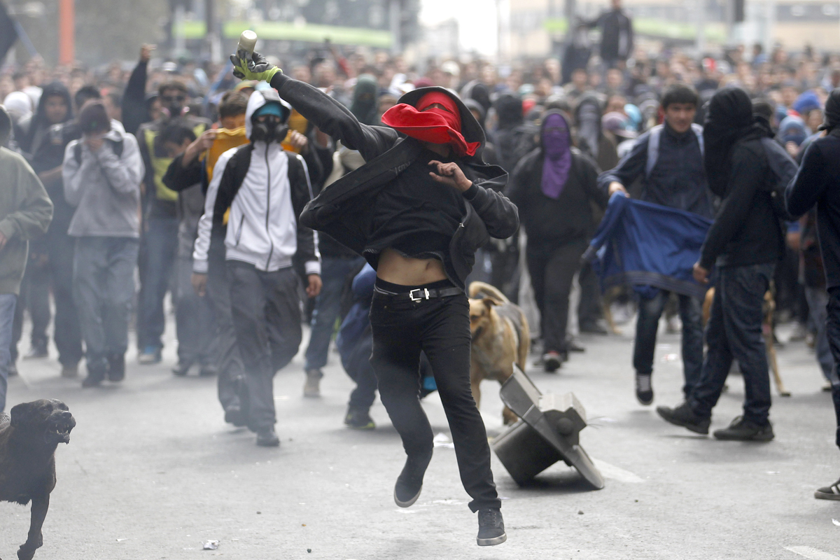 A student protester prepares to throw a bottle with paint at riot police officers during a rally in which demonstrators demanded that the government make changes to the public state education system, in Santiago April 11, 2013. Chilean students and t