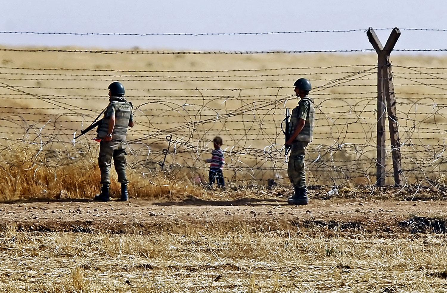 Szíriai gyermek a török határon lévő szögesdrót kerítésnél. A fegyveresek rá se hederítenek 